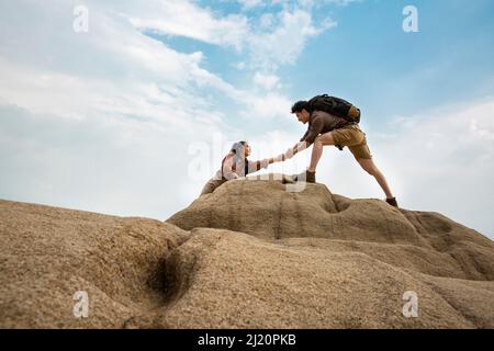 Gli alpinisti si allungano per aiutarsi l'un l'altro su ripidi cime rocciose, vista ad angolo basso - foto di scorta Foto Stock