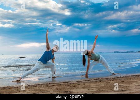 Giovane coppia che pratica lo yoga si allunga sulla spiaggia - foto di scorta Foto Stock