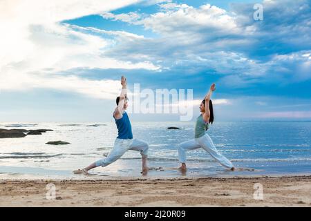 Giovane coppia che pratica lo yoga si allunga sulla spiaggia - foto di scorta Foto Stock