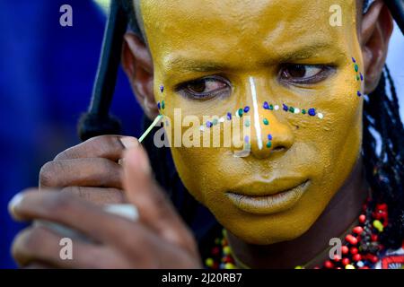 Uomo della tribù nomade di Wodaabe che dipinge faccia per la celebrazione di Gerewol, un raduno di clan differenti in cui le donne scelgono un marito. Abbigliamento uomo in bes Foto Stock