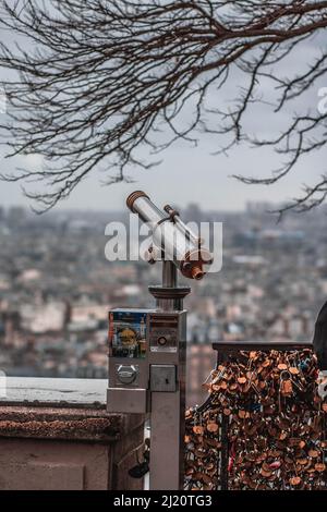 Un colpo verticale di un telescopio accanto alle serrature sul ponte che si affaccia sullo sfocato paesaggio urbano di Parigi Foto Stock