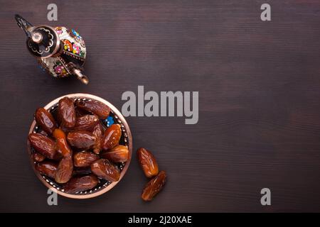 Piatto con datteri, caffettiera su tavolo di legno marrone scuro. Sfondo Ramadan. Vista dall'alto. Foto Stock