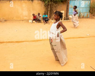 MBOUR, SENEGAL, AFRICA - DICEMBRE CIRCA, 2021. Bambini africani non identificati che fanno una corsa di sacco per strada. Devono riempire il bacino con w Foto Stock