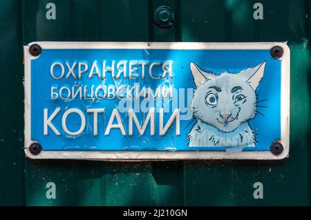 Kiev, Ucraina - 3 luglio 2021: Un cartello blu appisso sulla recinzione di fronte ad una casa suburbana. Il cartello recita "sorvegliato dai gatti da combattimento". C'è un disegno Foto Stock