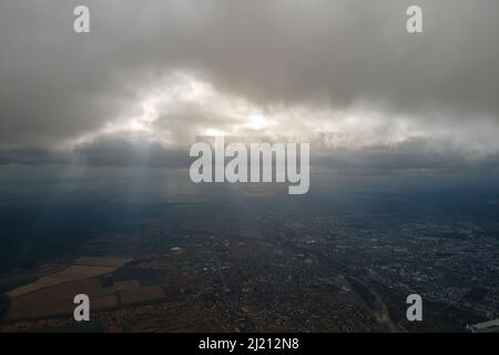 Vista aerea dalla finestra dell'aeroplano ad alta quota della città lontana coperta con strato di smog sottile e nubi distanti in serata. Foto Stock