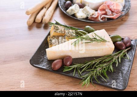 Antipasti italiani, tagliere di formaggi con selezione di formaggi e salumi con prosciutto servito con olive e grissini su piatto nero su legno Foto Stock