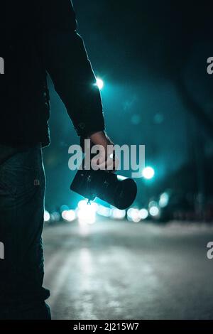 Una mano di un maschio che tiene una macchina fotografica per sparare di notte in su una strada vuota Foto Stock