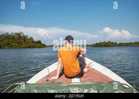 Vista posteriore dell'uomo seduto sulla prua della barca durante il viaggio sul lago, Sri Lanka Foto Stock