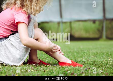 Trampolino salto incidente concetto. Ragazza bambino che tiene la caviglia spruzzata con le mani all'aperto dal trampolino del giardino domestico. Concetto di pericoli a casa. Foto Stock