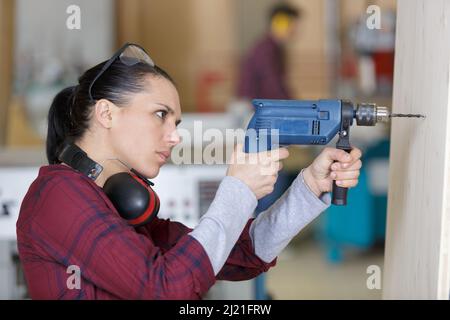 donna che fora in lamiera di legno in carpenteria Foto Stock