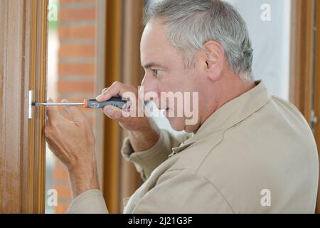 uomo con cacciavite avvitabile a cerniera su una porta Foto Stock