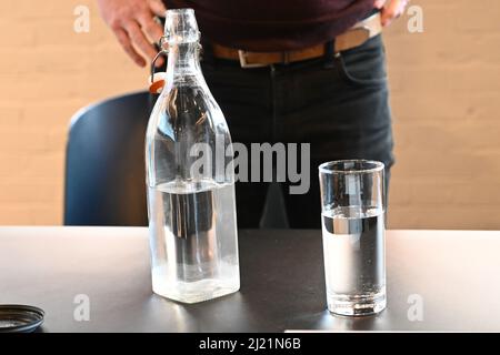 Una bottiglia d'acqua di vetro con un bicchiere quasi pieno d'acqua seduto su un tavolo nero Foto Stock