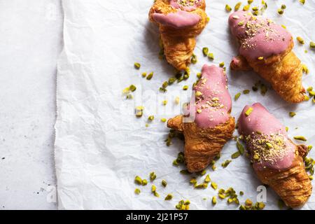 Mini croissant con cioccolato al rubino e pistacchi su carta da forno, sfondo grigio. Vista dall'alto e spazio di copia. Foto Stock