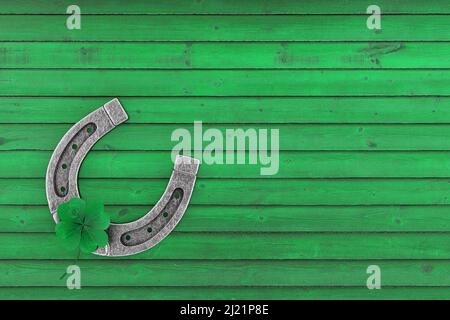 Old Steel Lucky Horseshoe con Green Clover Four Leaf su uno sfondo verde in legno. 3D rendering Foto Stock