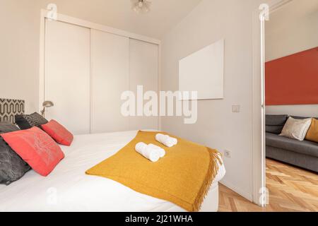 Camera da letto con letto king-size, armadio a muro con porte scorrevoli bianche, cuscini rossi e neri e coperta color senape Foto Stock