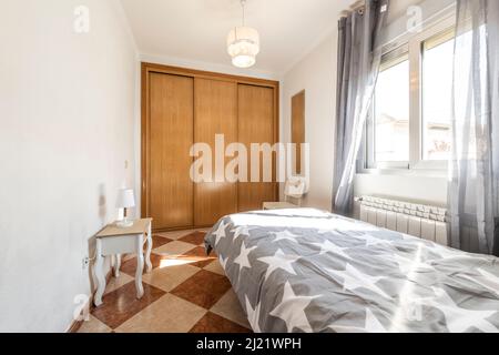 Camera da letto per giovani con comodino in legno bianco con trapunta grigia con stelle, armadio da incasso con tre porte scorrevoli e radiatore in alluminio un Foto Stock