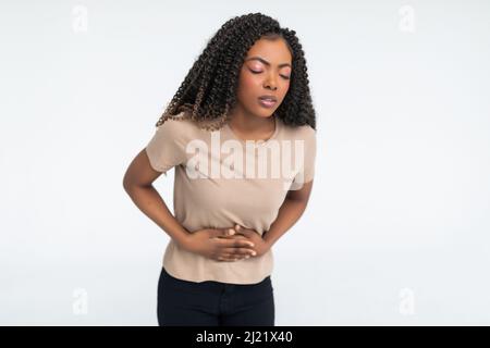 Ritratto di primo piano di giovane donna stressata, mettendo le mani sullo stomaco avendo dolori e dolori cattivi, isolato su sfondo bianco. Foto Stock