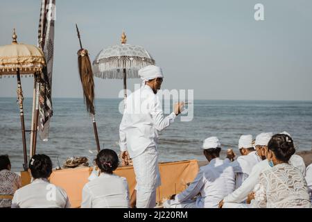 Indù balinese che prega presso l'oceano. Gli indù balinesi eseguono il rituale di purificazione, la cerimonia di Melasti prima di Nyepi, il giorno del silenzio a Bali Foto Stock