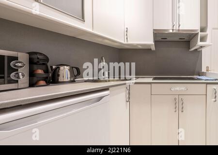 angolo cottura con mobili in legno bianco, piano di lavoro grigio, piccolo frigorifero bianco, macchina per il caffè e bollitore sul banco Foto Stock