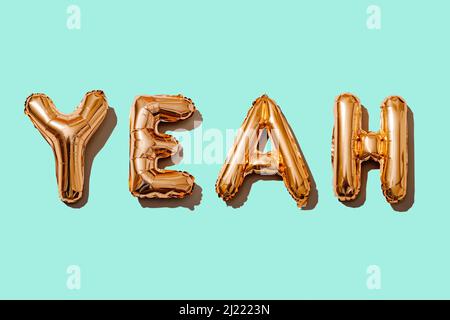 palloncini dorati a forma di lettera che formano la parola yeah su uno sfondo blu Foto Stock