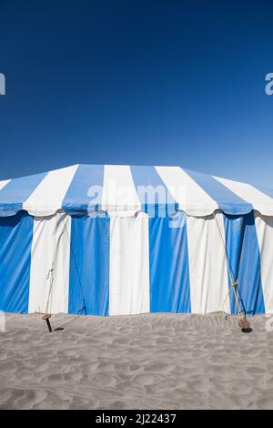 Una grande tenda a strisce blu e bianche o tendone su una spiaggia Foto Stock