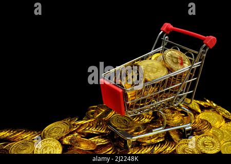 Monete d'oro nel carrello della spesa su una moneta d'oro impilabile su sfondo nero Foto Stock