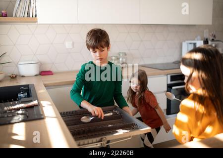 Tre piccoli chidlren aiutare con i piatti in cucina a casa. Foto Stock