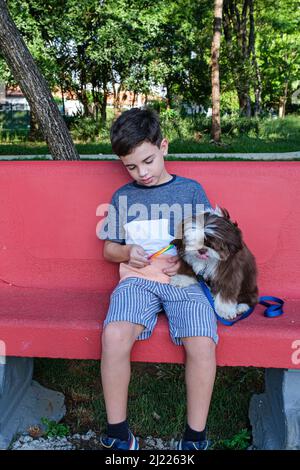 ragazzo di 8 anni seduto su una panca di cemento, offrendo il suo lecca alla sua foto pet vertical. Foto Stock