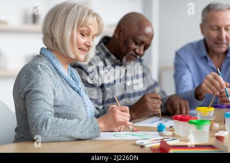 Signora anziana di buon aspetto che ama l'attività di pittura con i suoi amici Foto Stock