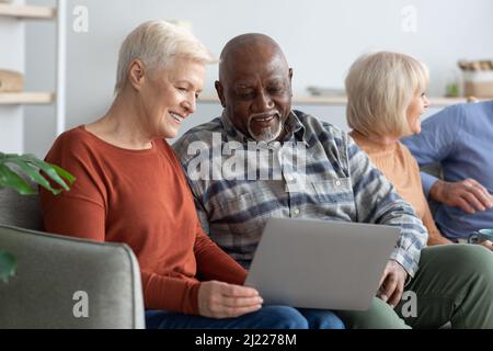 Sorridente uomo nero anziano e donna caucasica utilizzando un computer portatile Foto Stock