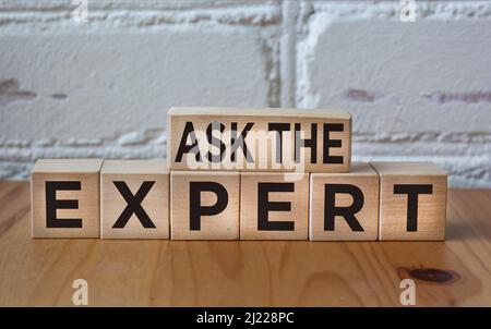 CHIEDERE ALL'ESPERTO scritto su blocchi di legno contro una parete di mattoni bianchi Foto Stock