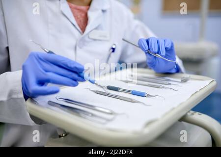 Strumenti dentistici a portata di mano. Primo piano di un dentista irriconoscibile che lavora con un vassoio di strumenti chirurgici. Foto Stock