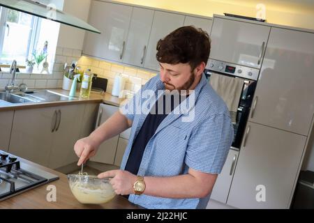 Uomo in cucina mescolare gli ingredienti della pastella in un recipiente di miscelazione Foto Stock