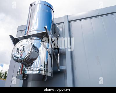 il tubo del camino entra nel muro. Tubo lucido sulla parete blu. Pipeline nell'area di produzione. Tubazioni in acciaio inox. Frammento di sistema di camino. engi industriale Foto Stock