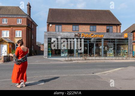 Donna in abito arancione all'esterno di un negozio di angolo per animali domestici con cartello arancione corrispondente nel villaggio di Greyshott, Hampshire, Inghilterra, Regno Unito Foto Stock