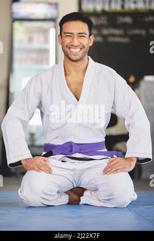 Orgoglioso dei miei progressi. Ritratto a tutta lunghezza di un bel giovane uomo inginocchiato in pieno jiu jitsu gi in palestra. Foto Stock