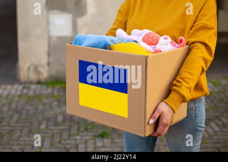 I volontari tengono nelle loro mani una scatola di aiuti umanitari con cose e giocattoli per bambini per le necessità degli ucraini per strada. Aiuto per l'Ucraina Foto Stock