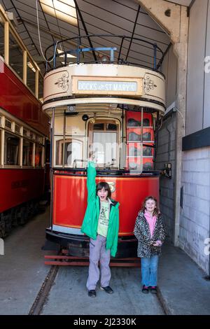 Derbyshire, Regno Unito – 5 aprile 2018: Due bambini posano di fronte a un tram d'epoca immagazzinato nel garage del Crich Tramway Village Foto Stock