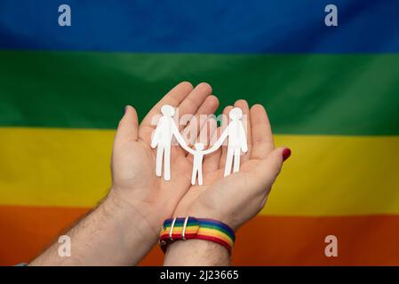 mani di uomo con famiglia di carta gay su sfondo lgtb arcobaleno bandiera Foto Stock