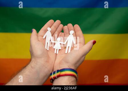 mani di uomo con famiglia di carta gay su sfondo lgtb arcobaleno bandiera Foto Stock