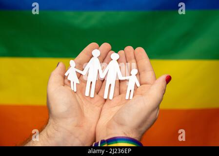 mani di uomo con famiglia di carta gay su sfondo lgtb arcobaleno bandiera Foto Stock