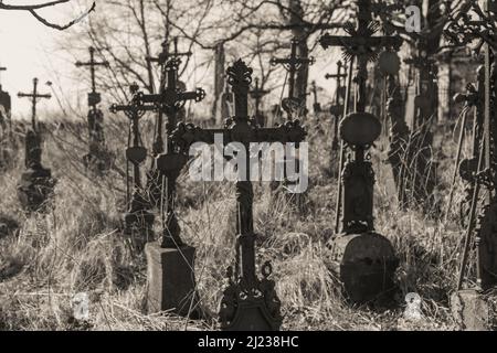 Un primo piano di croci del cimitero circondato da erba secca in scala di grigi Foto Stock