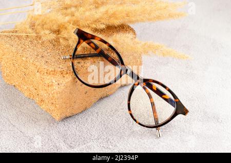 Occhiali eleganti su un podio in pietra naturale. Occhiali e piante di leopardo su sfondo concreto Foto Stock