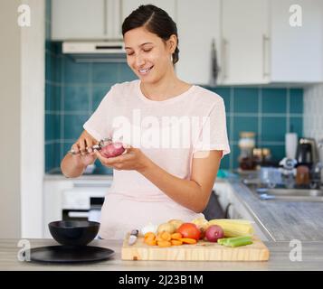 Pelare i veggies mi porta la pace. Shot di una giovane donna che si sbuccia una patata nella sua cucina. Foto Stock