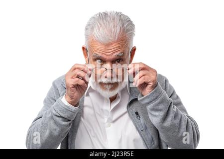 Un uomo anziano ed elegante in occhiali con barba e capelli grigi guarda da sotto la fronte e tiene gli occhiali con le mani. Foto Stock