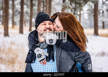 Donna Kissing uomo da dietro in una foresta di pino Snowy Foto Stock