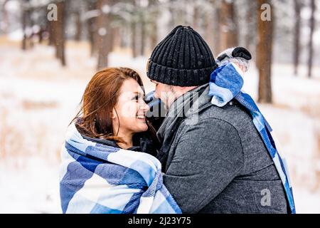 Coppia avvolta in una coperta blu in una foresta di Snowy Pine Foto Stock