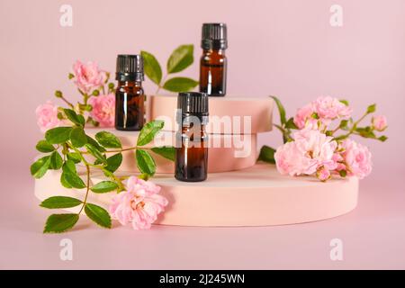 Rosa essenziale Oil.Aromatherapy e cosmetici. Set di bottiglie in vetro marrone e fiori di rosa su un podio rosa su olio di rosa naturale background.Organic rosa Foto Stock