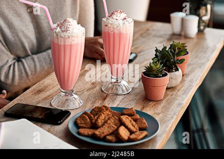 Fuori per alcuni rinfreschi. Scatto corto di una donna irriconoscibile che ha un milkshake e biscotti con la sua amica in un caffè. Foto Stock