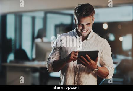 Niente guida il successo come il massimo impegno. Scatto di un giovane uomo d'affari che utilizza un tablet digitale in un ufficio di notte. Foto Stock